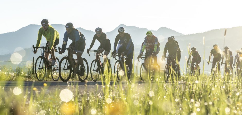 Mehrere Radsportler fahren mit dem Fahrrad ein Rennen. Im Hintergrund sieht man die Silhouette der Allgäuer Alpen. © ueberall.Deutschland